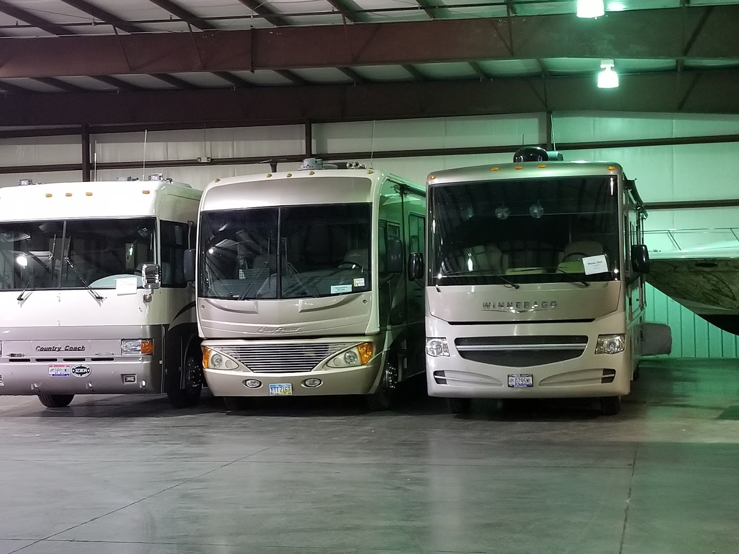 Three large Class-A motorhomes parked side-by-side inside a heated indoor storage warehouse