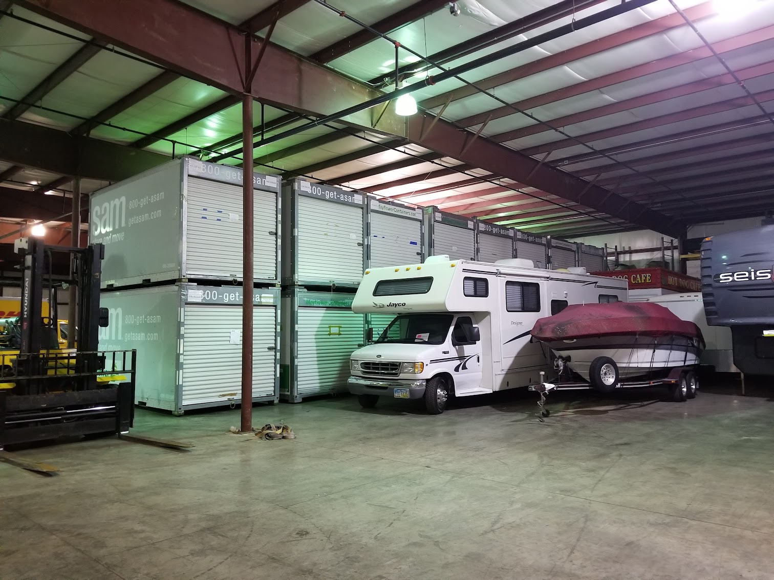 A Jayco motorhome and a covered boat on a trailer stored indoors next to stacked portable containers